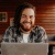 a man smiling while sitting at a desk with a laptop